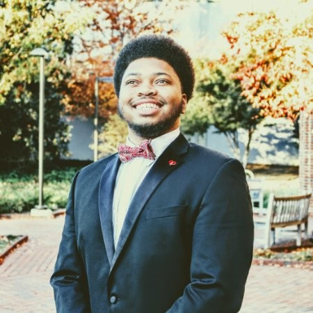 Jalen, a black, college-aged young man in bow tie & suit smiling on campus