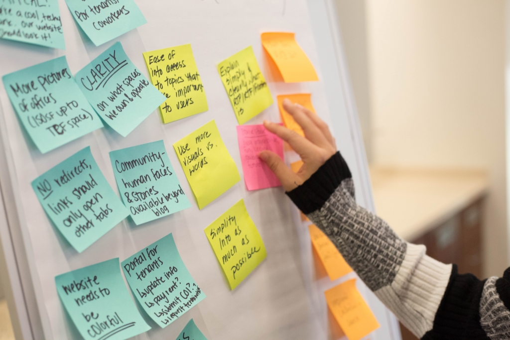 a woman's hand putting up a sticky note onto a white board covered with colorful sticky notes 